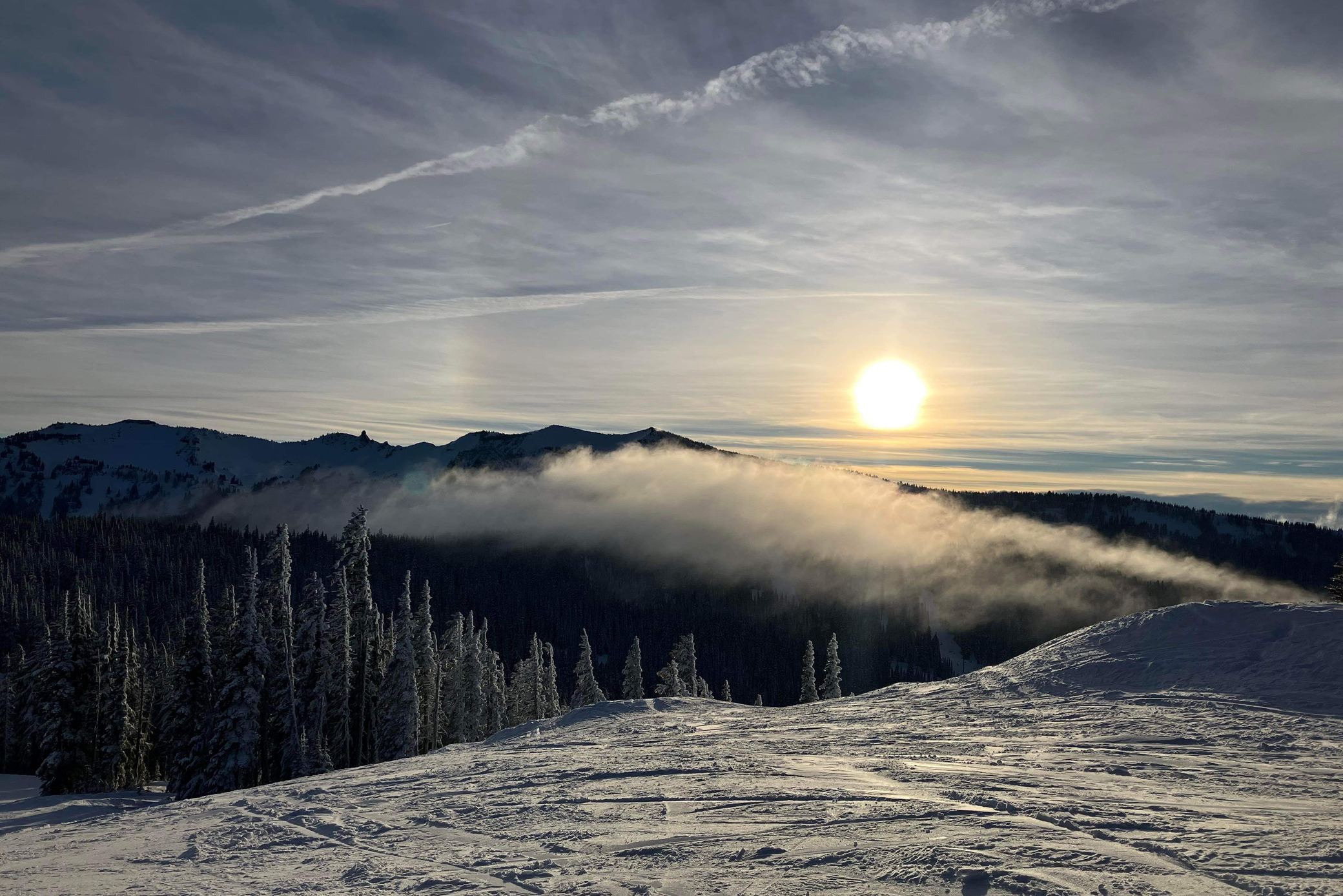 Low winter sun over a cloud inversion at White Pass, with snow-covered trees and freshly groomed runs in the foreground